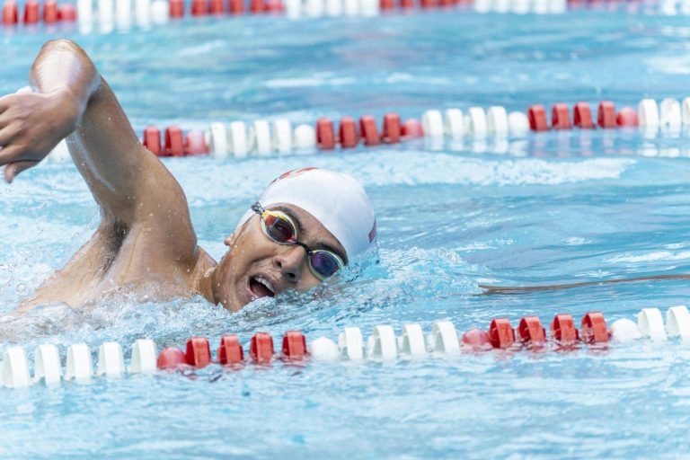 Male swimmer performing freestyle stroke in a pool, showcasing athleticism and skill.